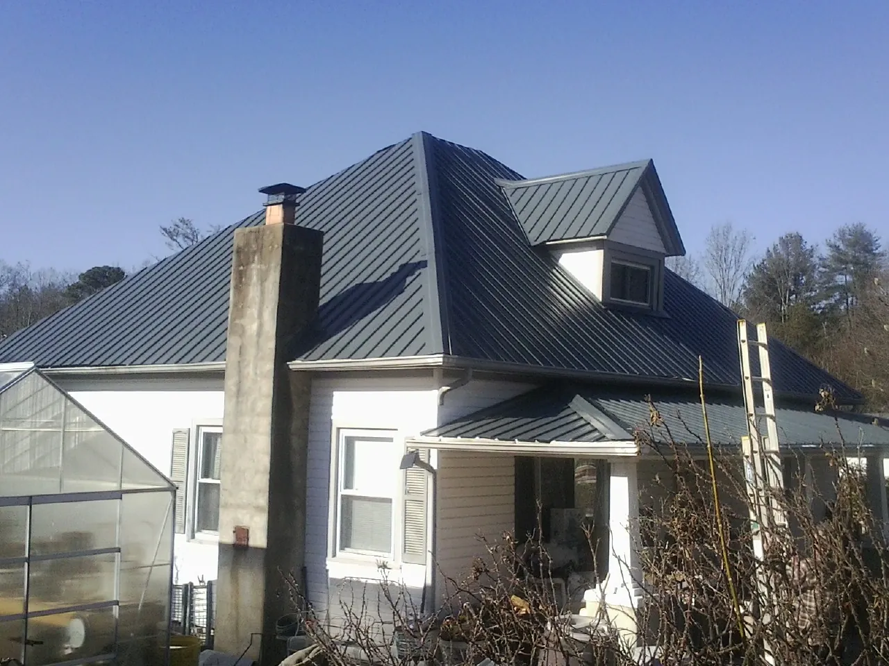 Dark blue standing seam metal roof on a white farmhouse with dormer — Slate & Tile Roof Repair by Roofing Brothers in Oakridge
