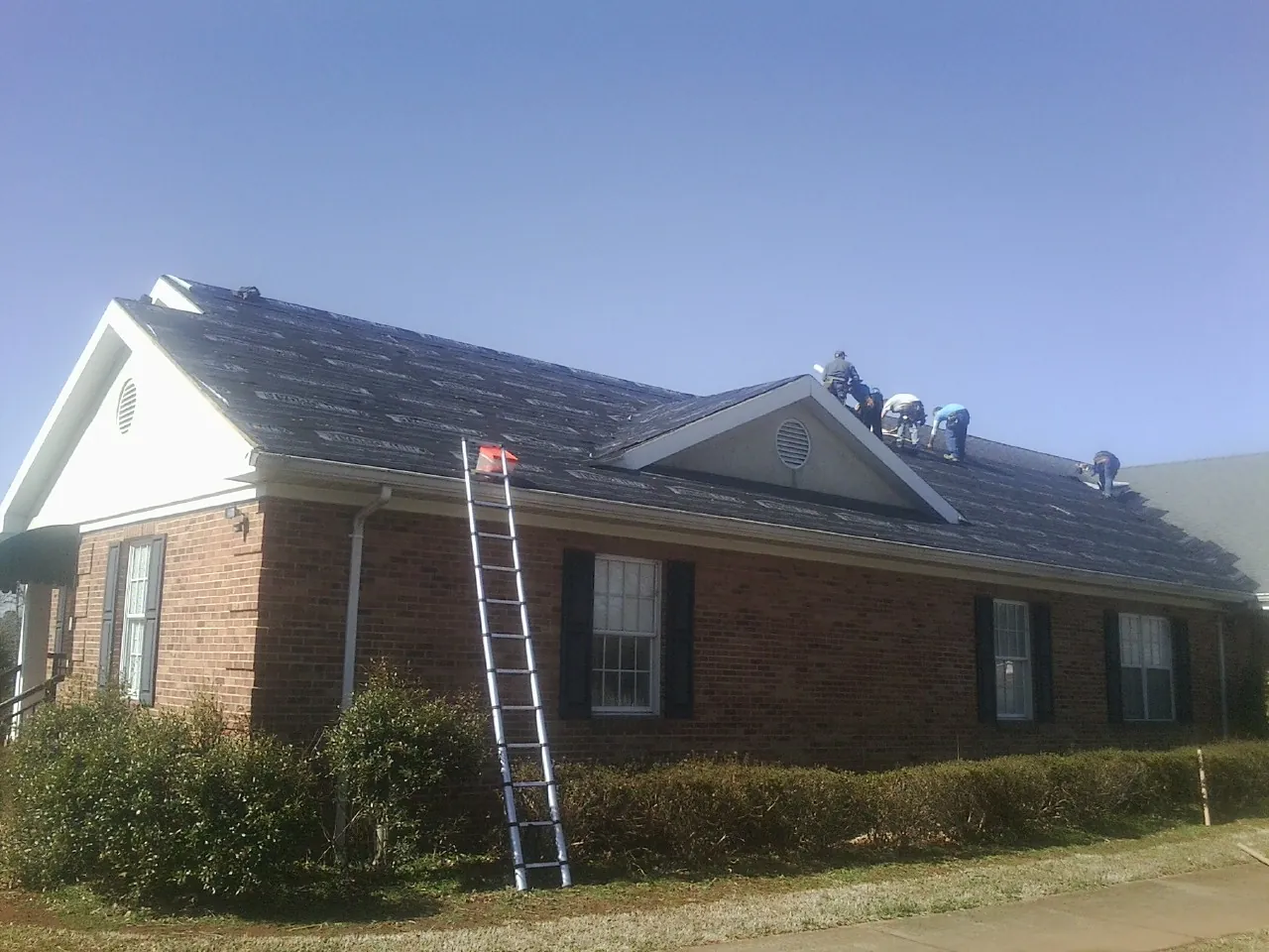 Crew tearing shingles off a brick ranch roof with a ladder set — Emergency Roof Repair work by our crew in Oakridge