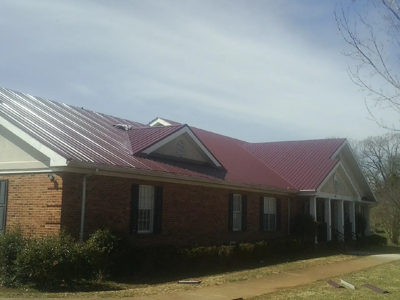 Red metal roof with gabled entries on a long brick building, from a Hail Damage Roof Repair job in Oakridge