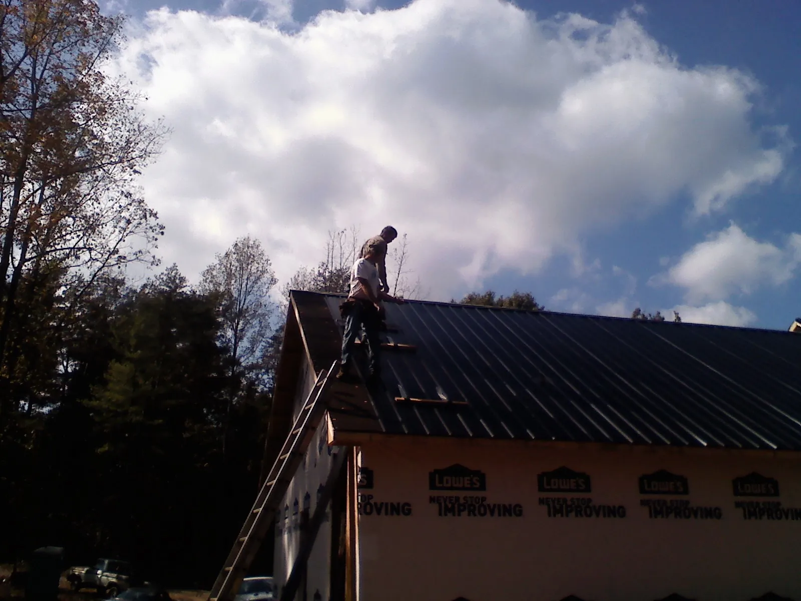 Roofer fastening dark metal panels high against a cloudy sky, from a Roof Inspection job in Oakridge