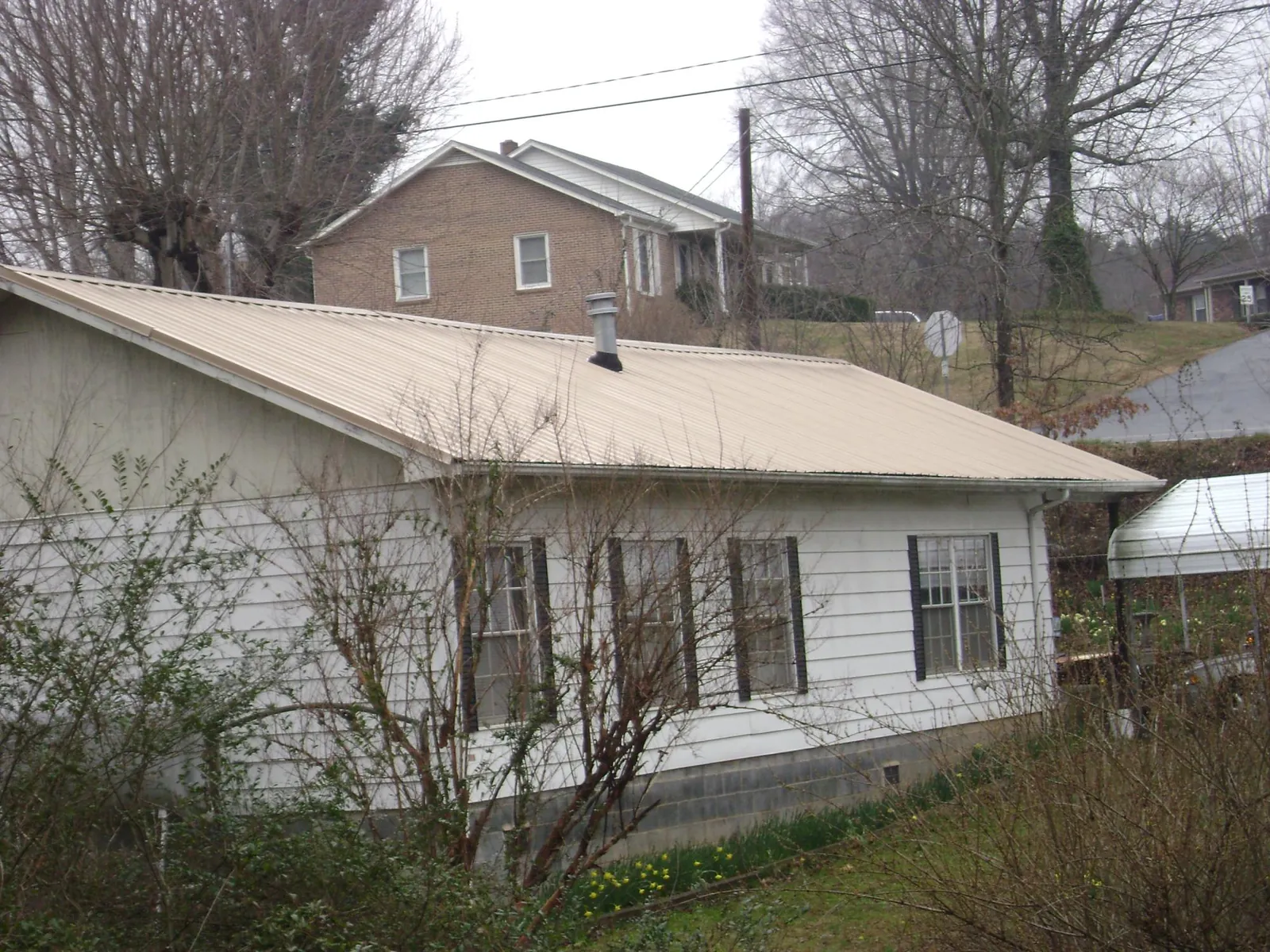 Tan metal roof on a white sided house set into a hillside — Commercial Roofing by Roofing Brothers in Oakridge