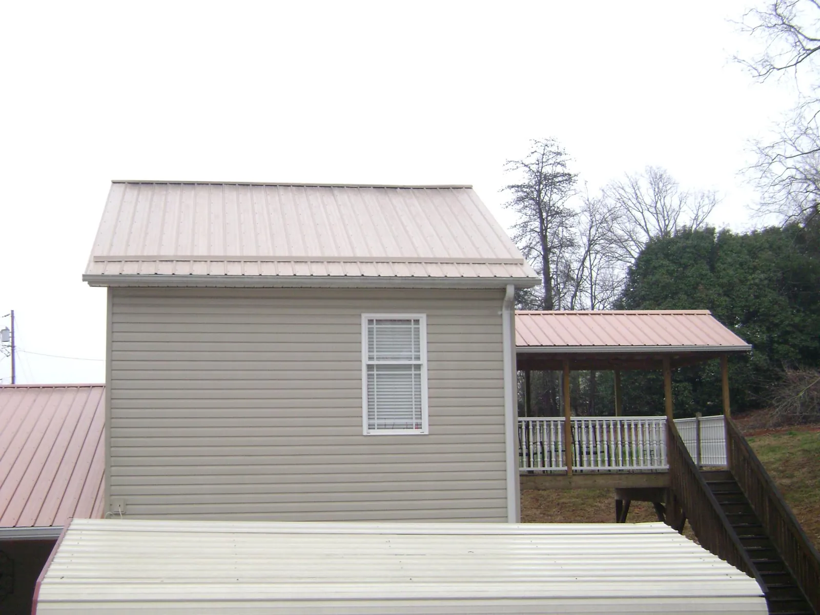 Tan metal roofs on a two story addition and attached porch, from a Roof Replacement job in Oakridge